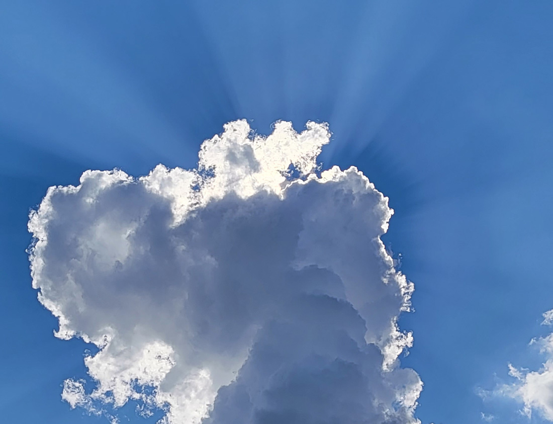 Scenic shot of the sun shining behind clouds showing rays of light and shadow emerging in the sky
