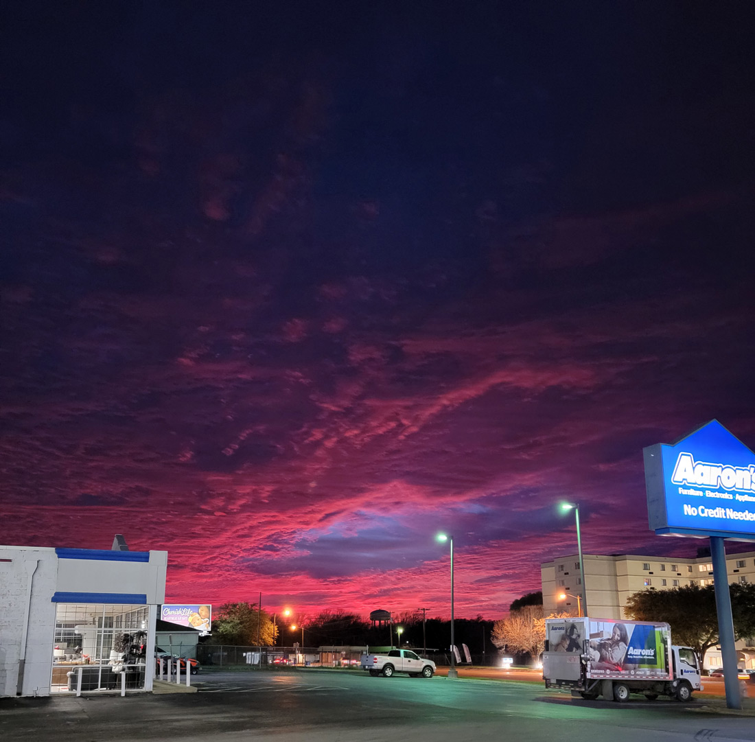 Scenic landscape shot of the sun setting creating a pink and purple sky over a shopping center
